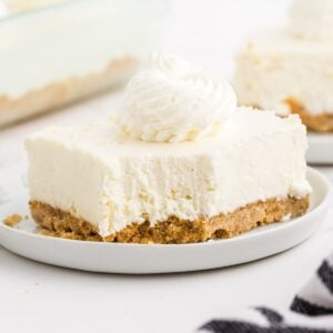 A no bake cheesecake bar with whipped cream on a plate.