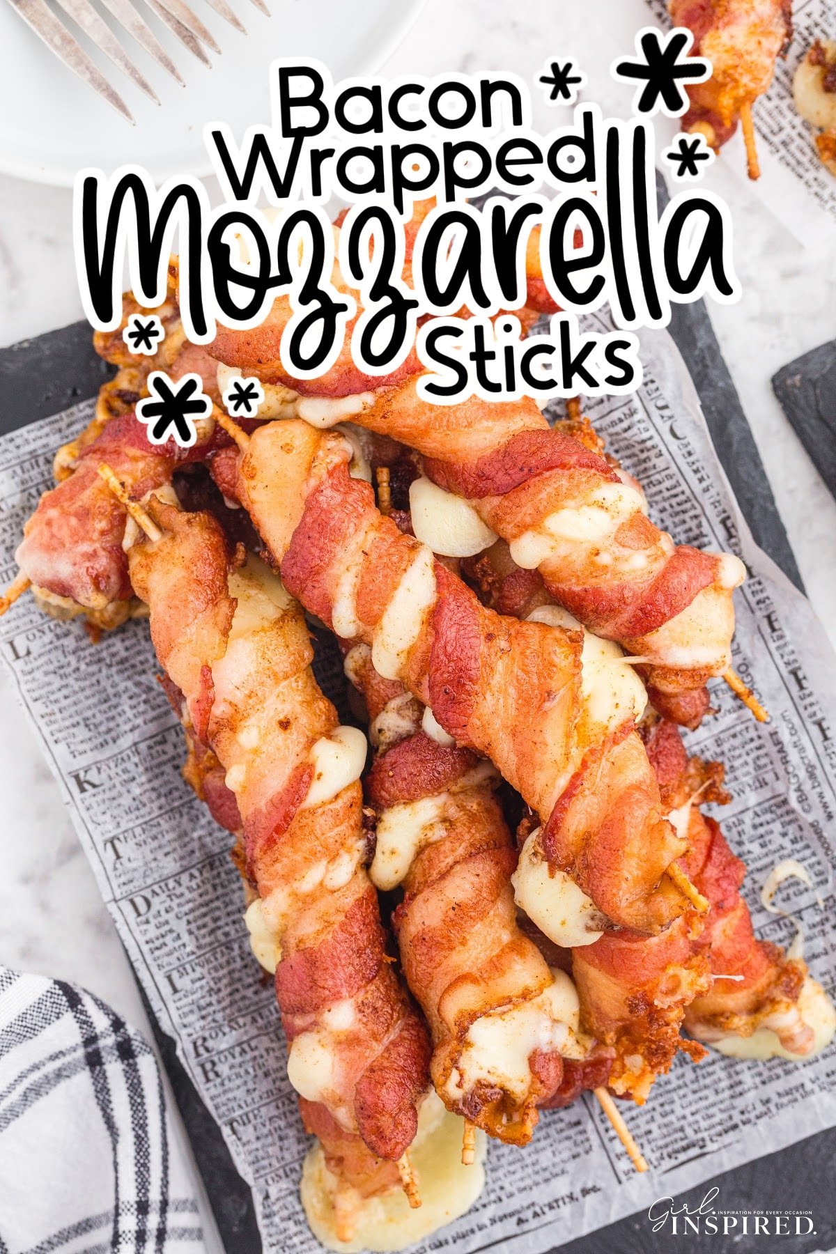 Bacon wrapped mozzarella sticks on a paper lined serving board with text overlay.