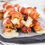 Bacon wrapped mozzarella sticks after being fried on a serving board.
