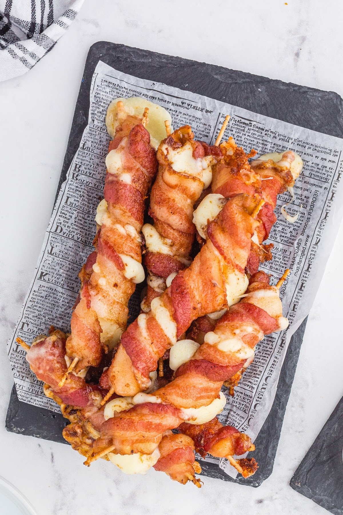 A batch of bacon wrapped mozzarella sticks on a serving tray.