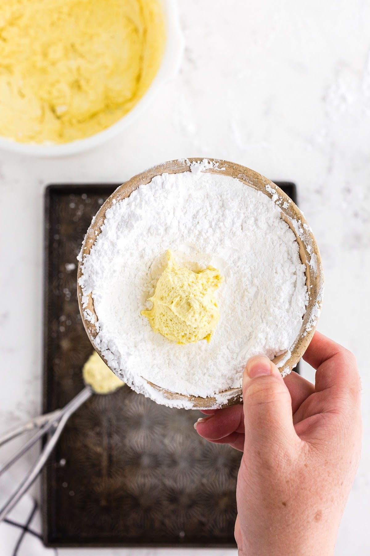 A lemon cool whip cookie being rolled in powdered sugar.