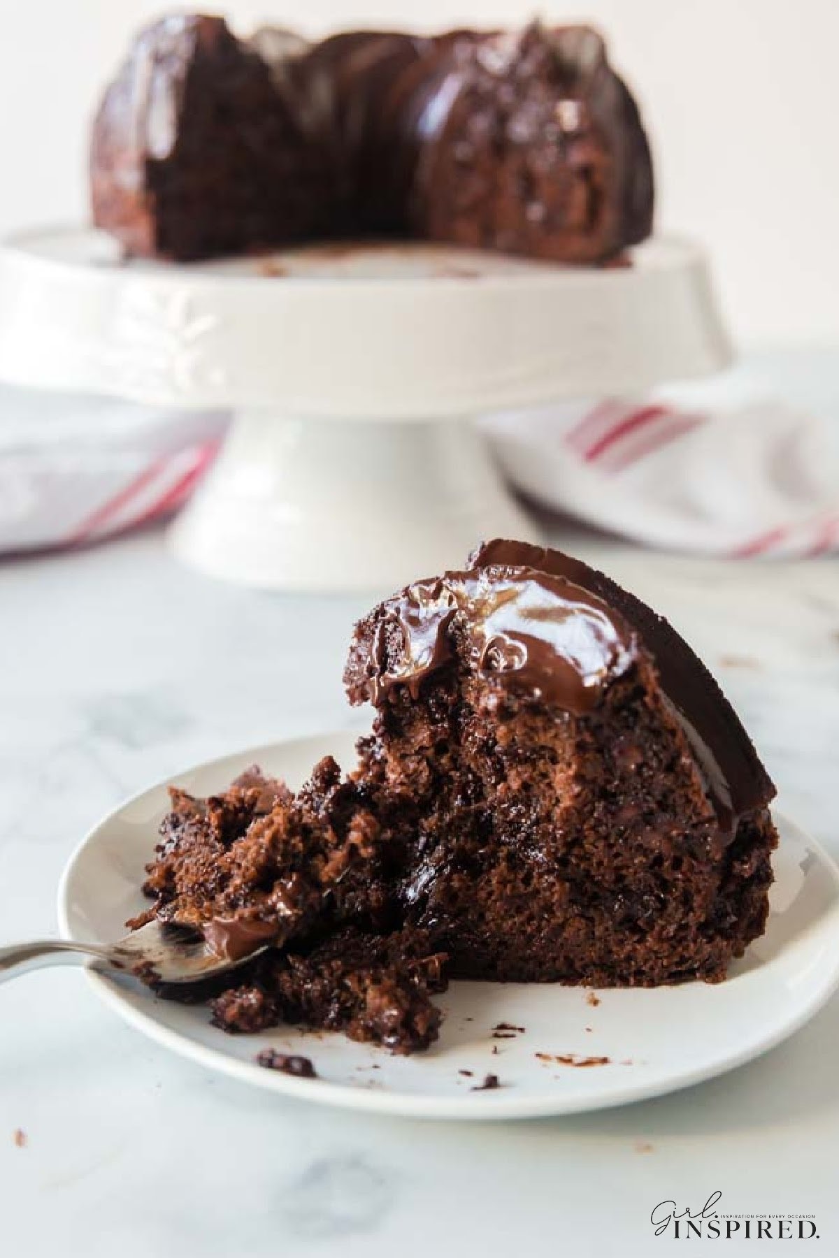 Two images of Double Chocolate Fudge Cake one on a cake platter and one on a plate with a bite missing.