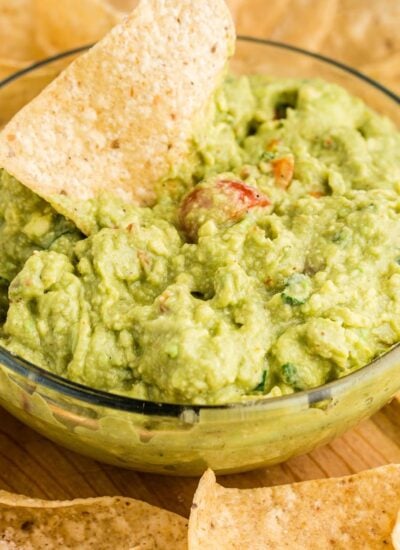 A large bowl of guacamole with a chip dipping into it.