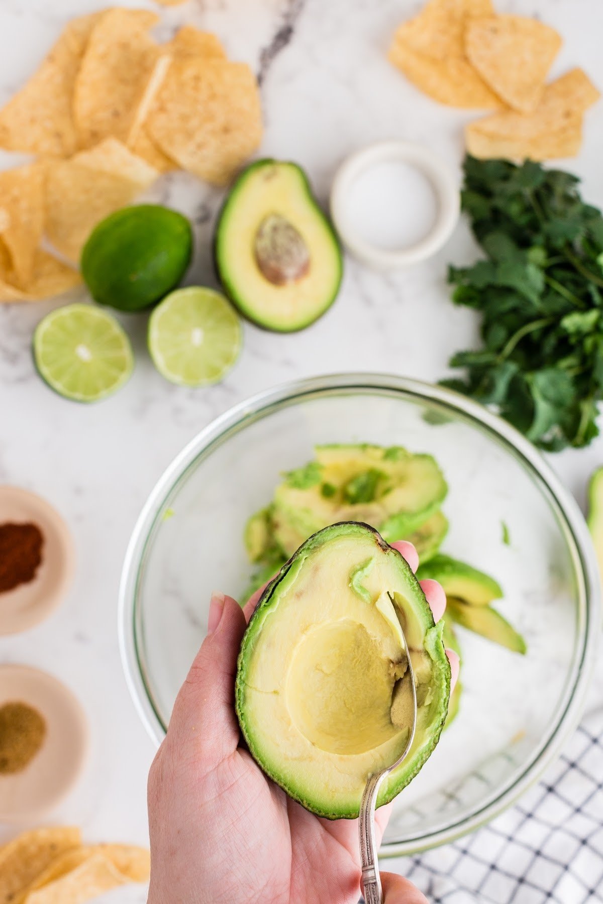 Large bowl with avocado being scooped into it, with ingredients off to the side too.