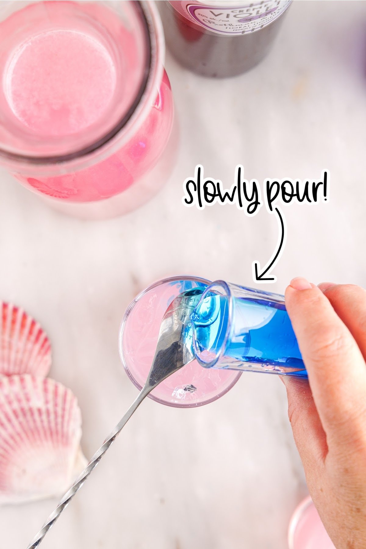 Pouring the blue liquor onto the back of a spoon into the pink lemonade.