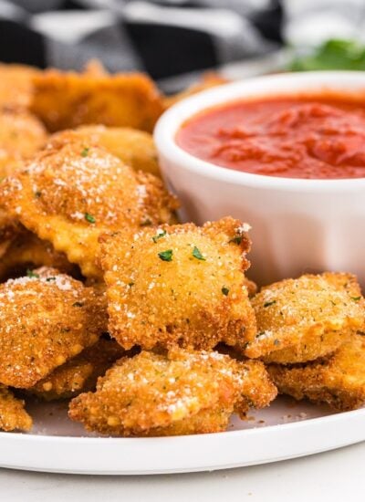 Fried raviolis on a platter with dipping sauce.