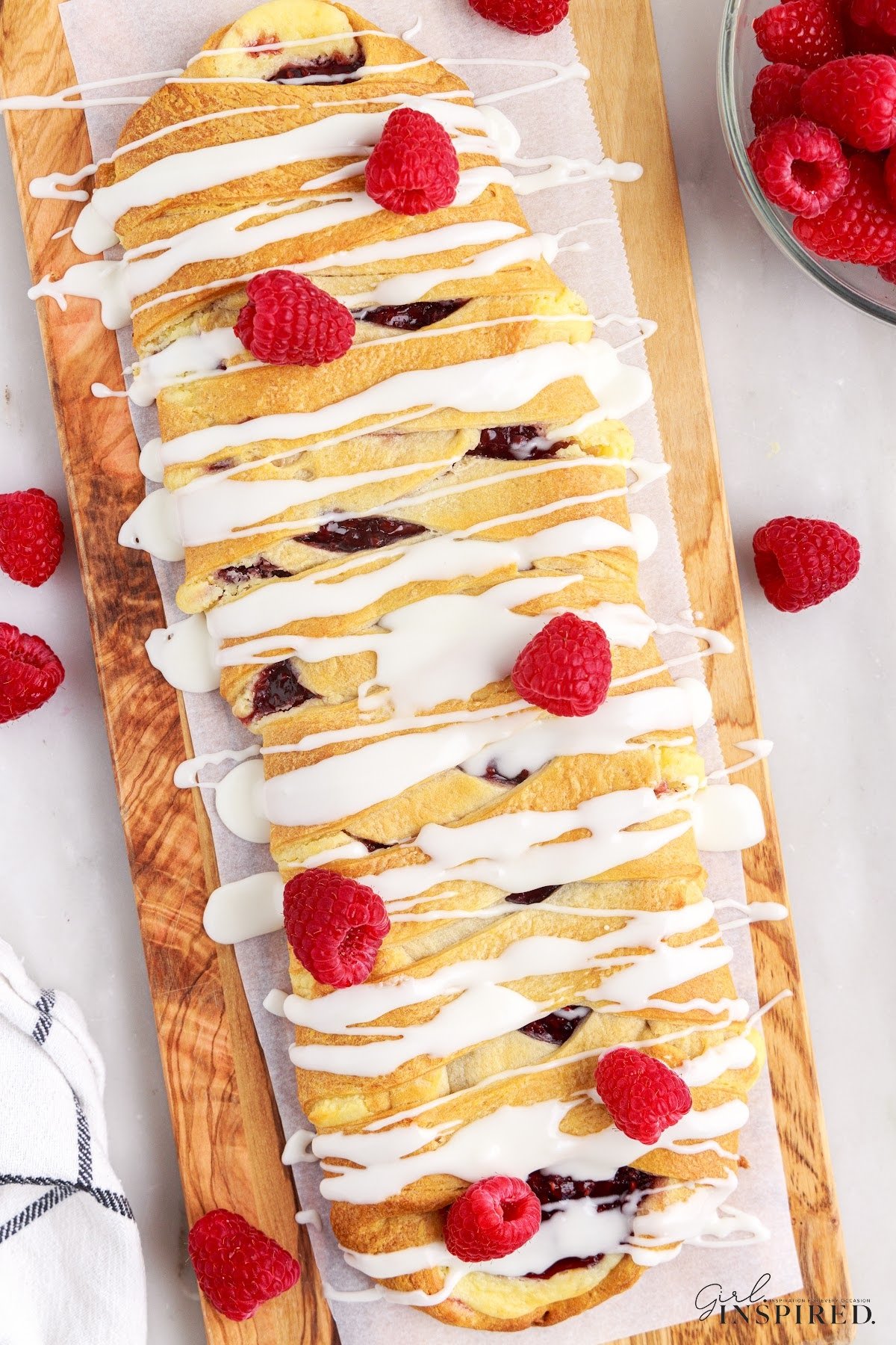 Raspberry cream cheese danish breakfast braid on a cutting board, ready to slice and serve.