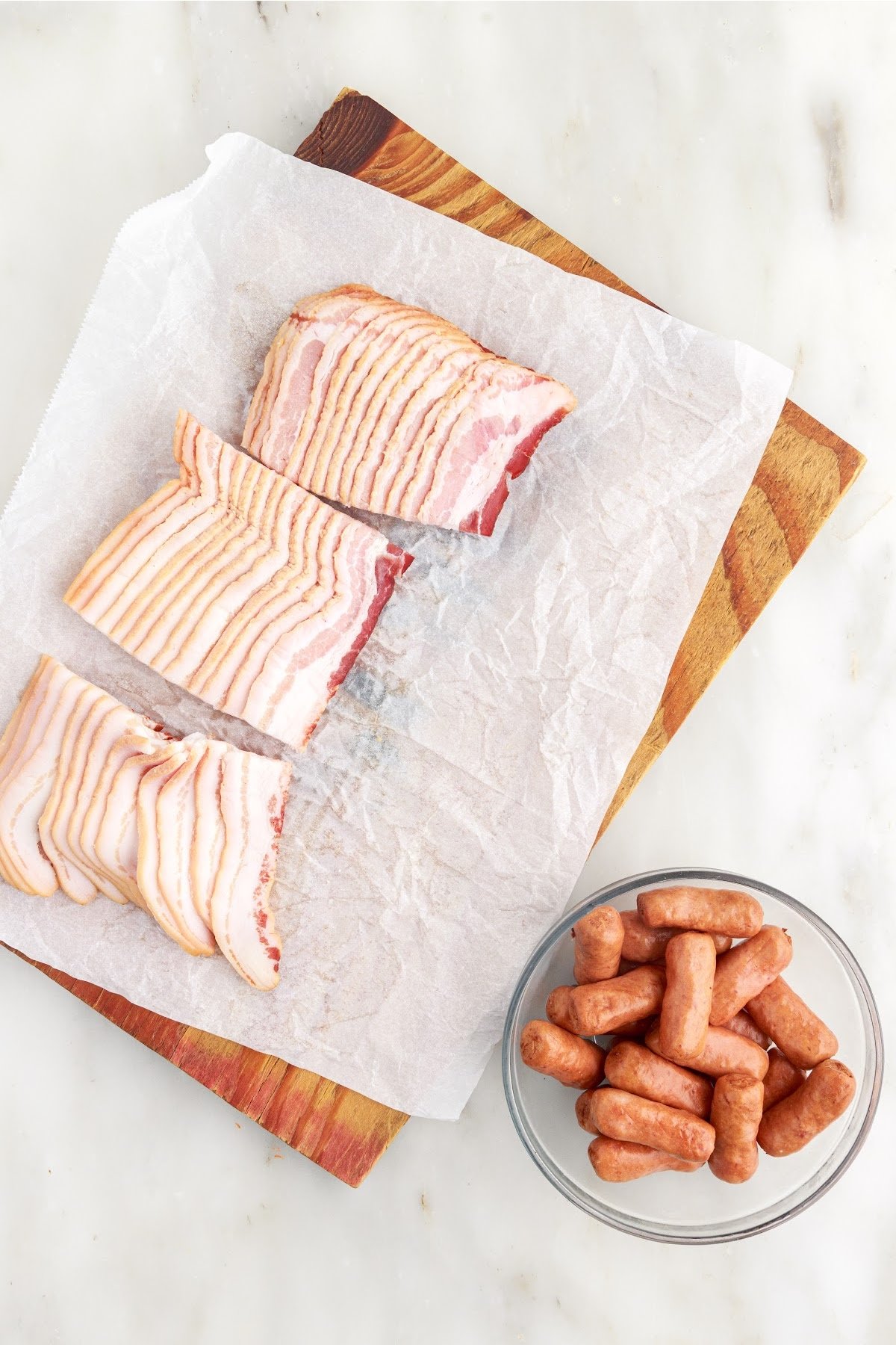 Bacon on a parchment covered cutting board and a bowl of little smokies.