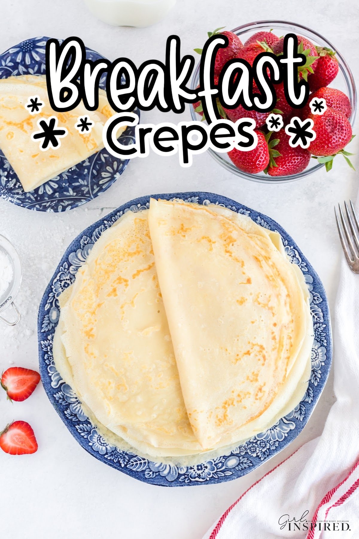 A stack of breakfast crepes on a plate next to a bowl of whole strawberries and a fork.
