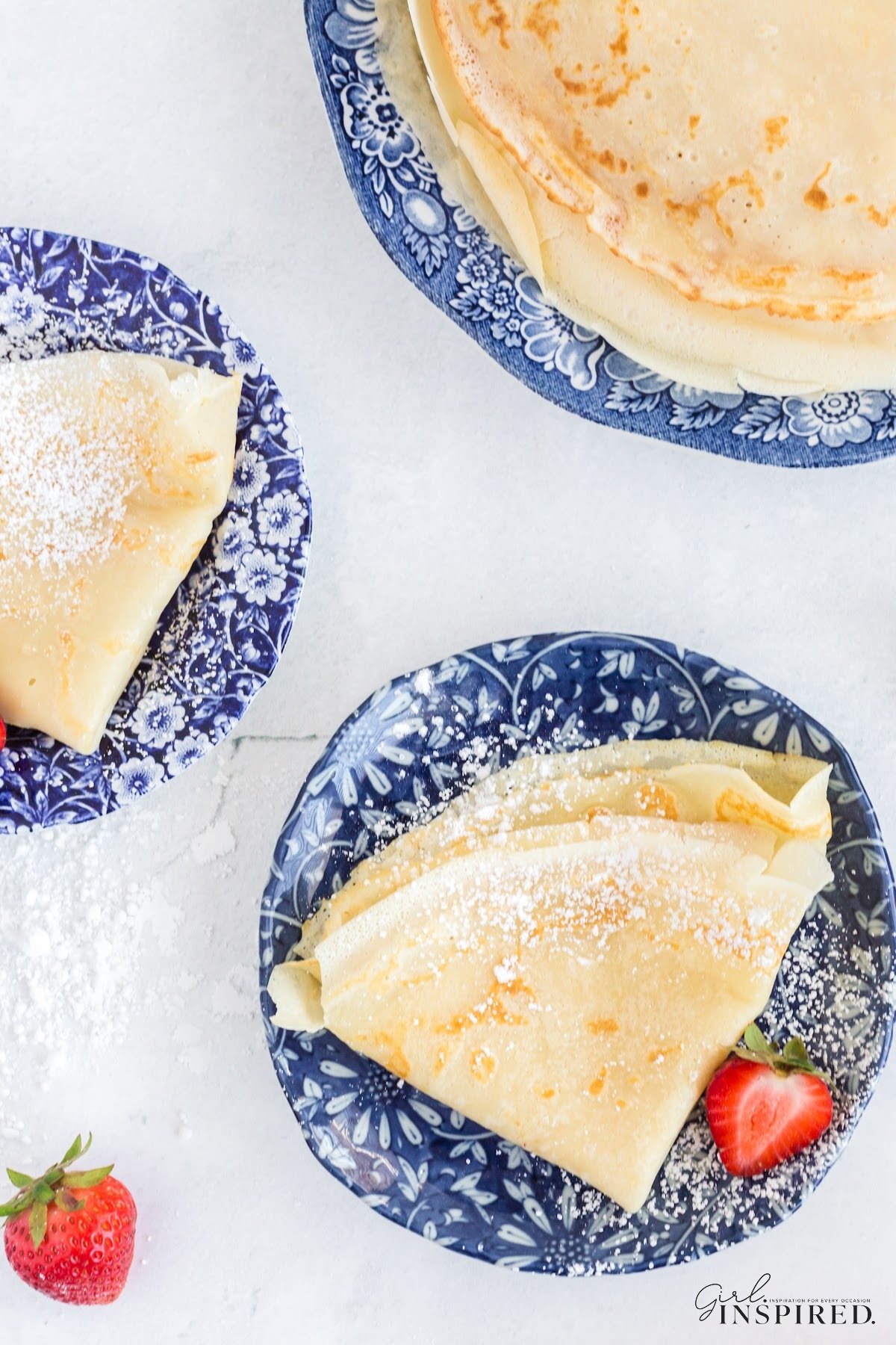 Folded breakfast crepes on plates dusted with powdered sugar.