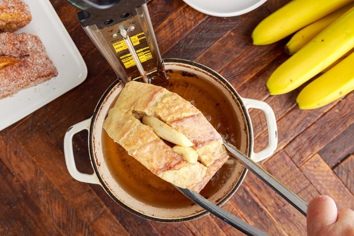 Placing the banana stuffed bread into the oil in the pan to fry.