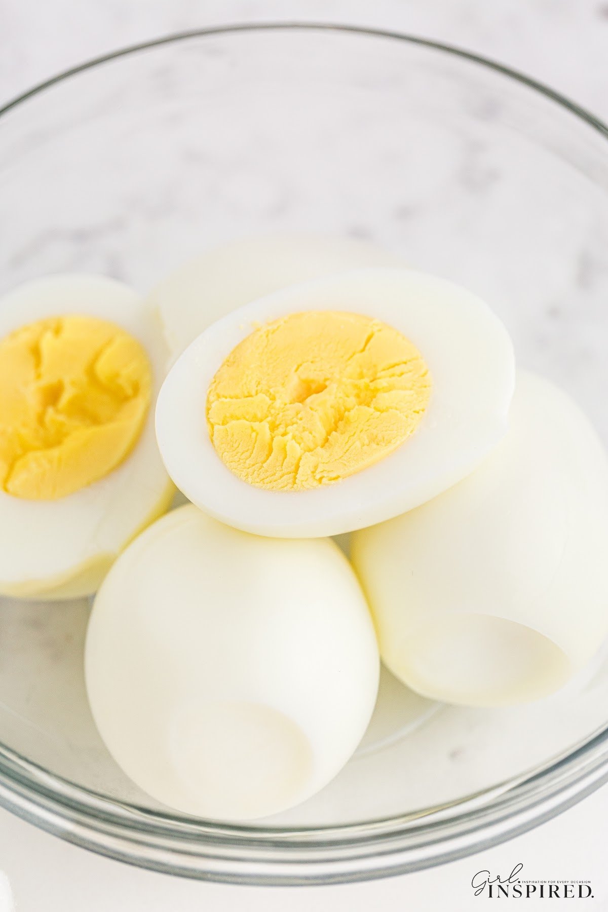 Bowl of Air Fryer Hard Boiled eggs, one cut open to see the yokes.