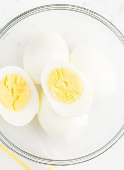 Bowl of Air Fryer Hard Boiled eggs, one cut open to see the yokes.