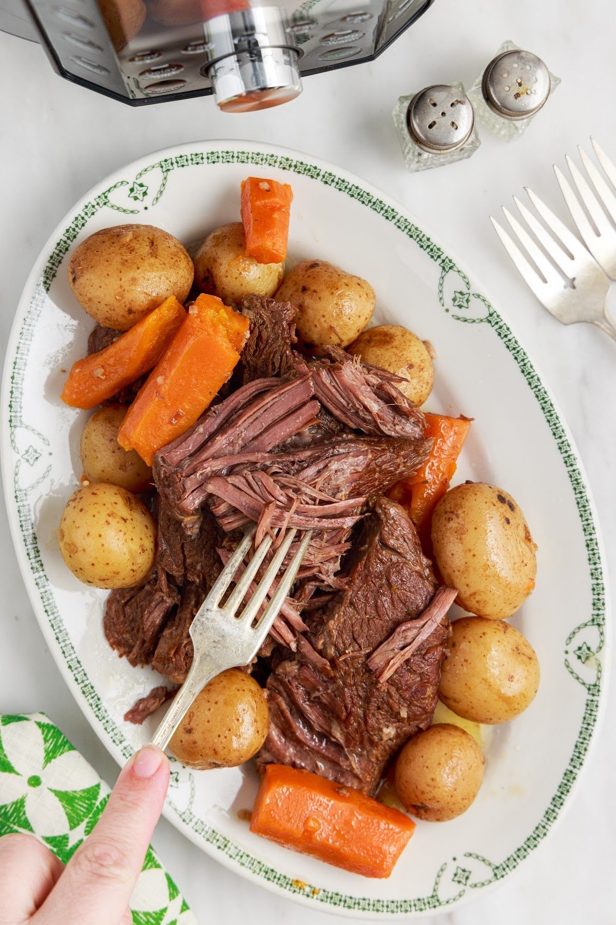 Shredded roast surrounded by potatoes and veggies, on a platter.