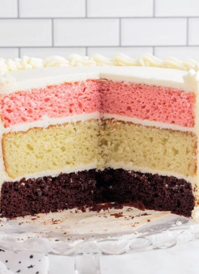 Neapolitan Cake frosted with white frosting, sliced open showing the layers.