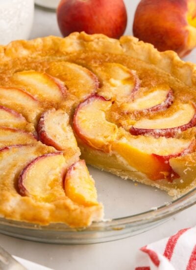 Homemade peach custard pie with slice missing in a glass pie dish.