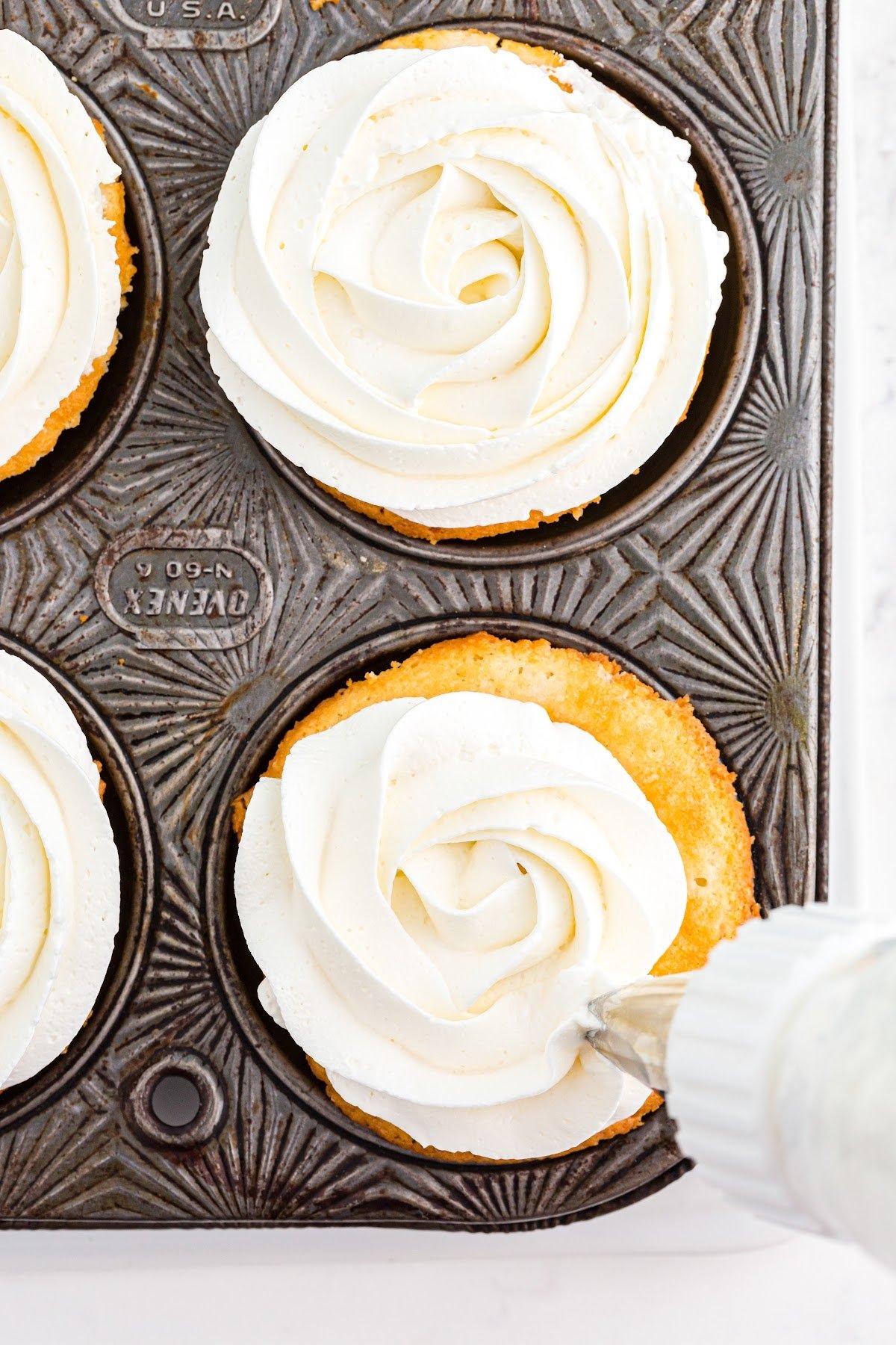 Frosting the cupcakes with white frosting.
