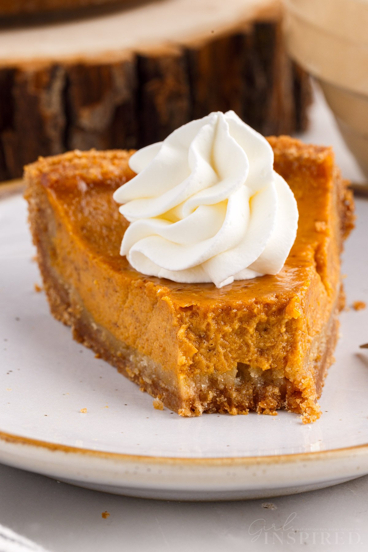 Pumpkin pie on graham cracker crust topped with whipped cream with a bite taken out.