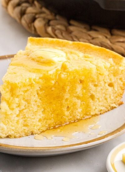 A slice of Buttermilk Cornbread Skillet on a plate being drizzled with honey on top.