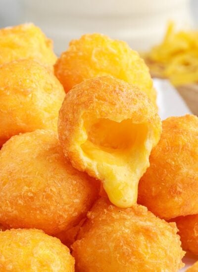 A pile of Fried Cheese Balls with one opened on the top to show the melted cheese.