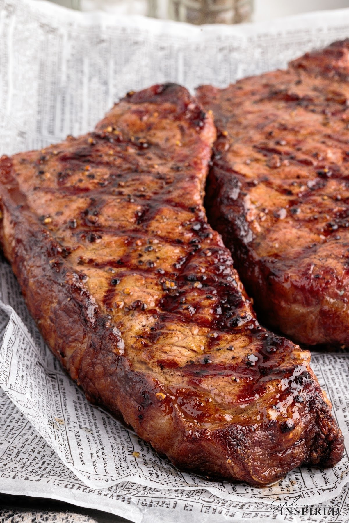 Two grilled New York strip steaks resting after coming off the grill.