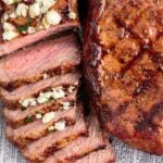 Two grilled New York strip steaks with one being sliced and topped with garlic butter.