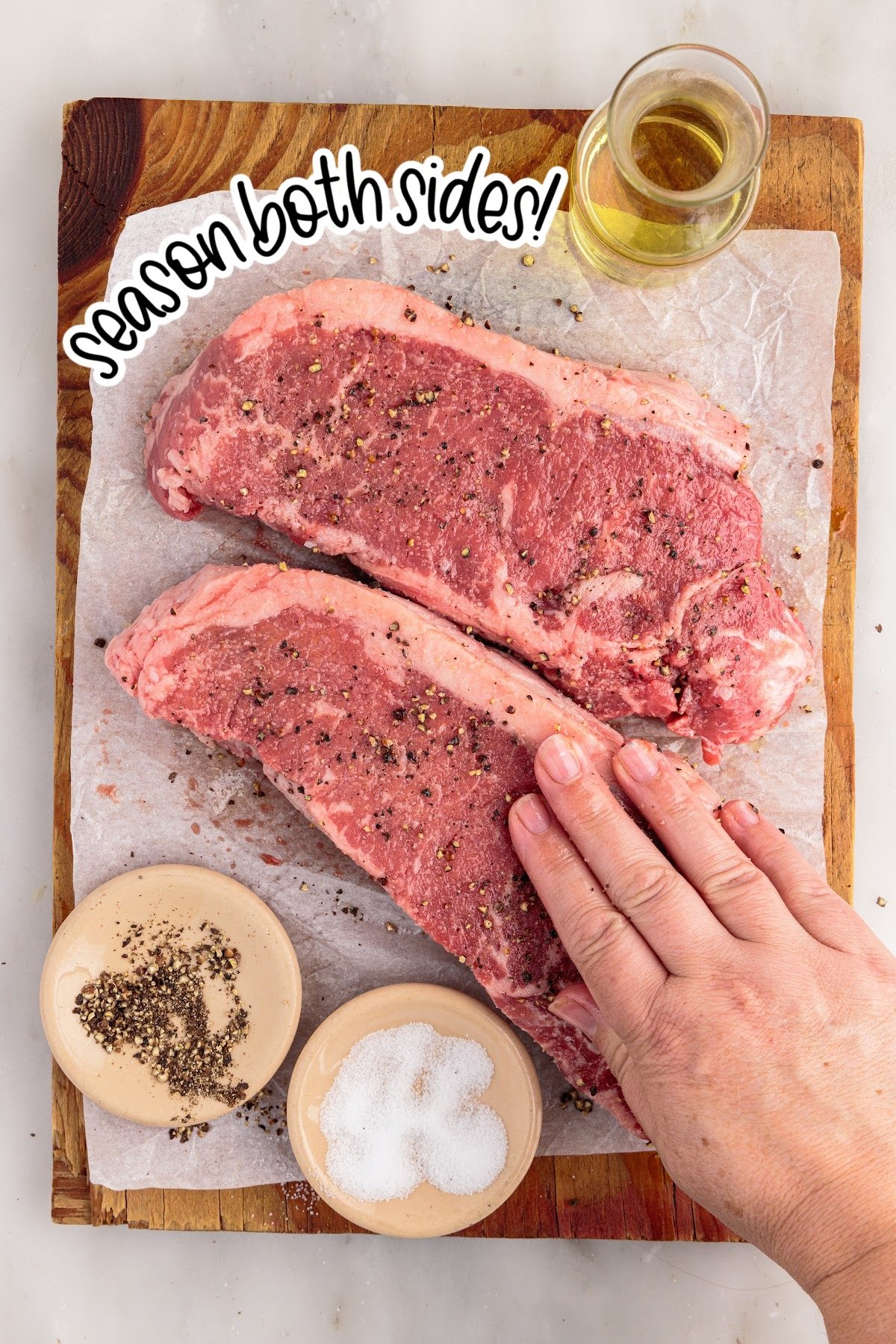 Seasoning two raw New York strip steaks.