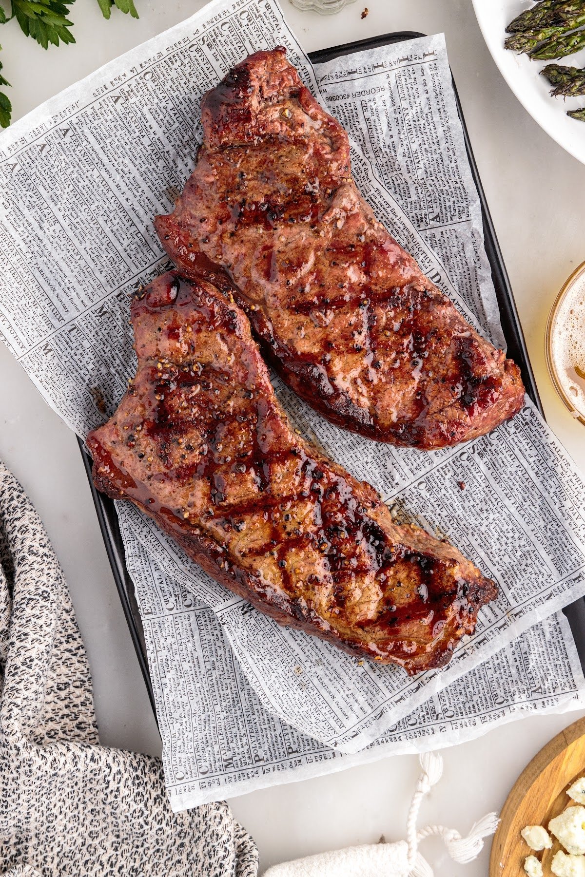 Two grilled New York strip steaks resting on parchment paper.