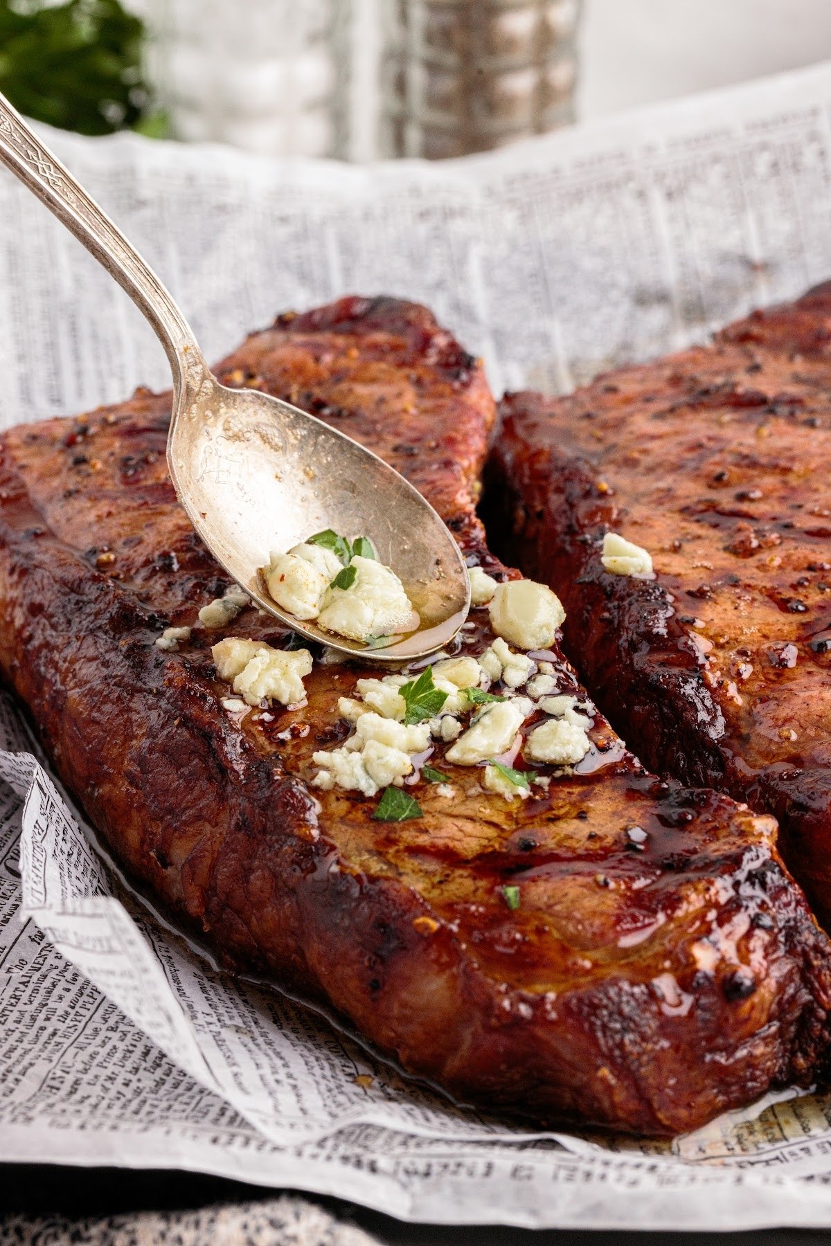 Spooning sauce over top of the grilled New York strip steaks.