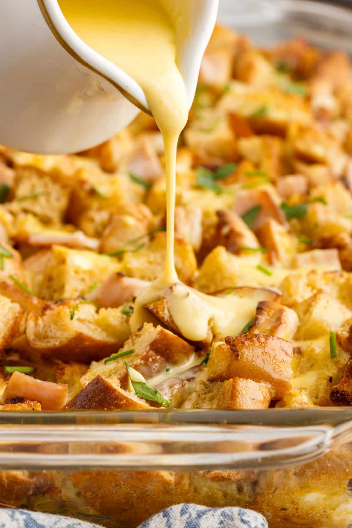Drizzling hollandaise sauce over eggs Benedict casserole.