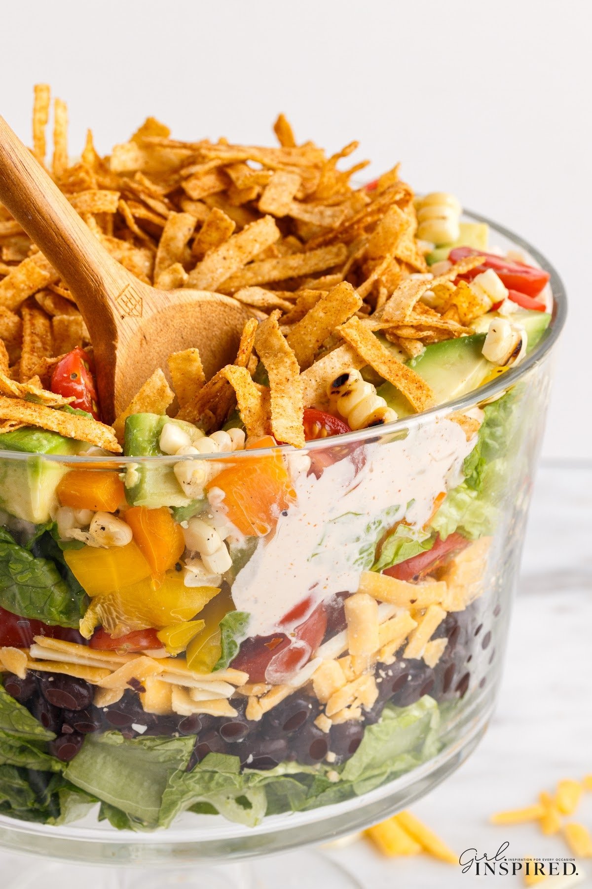 Layered Mexican salad with a wooden spoon in the bowl.