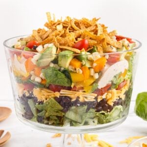 Layered Mexican salad topped with tortilla strips in a trifle bowl.