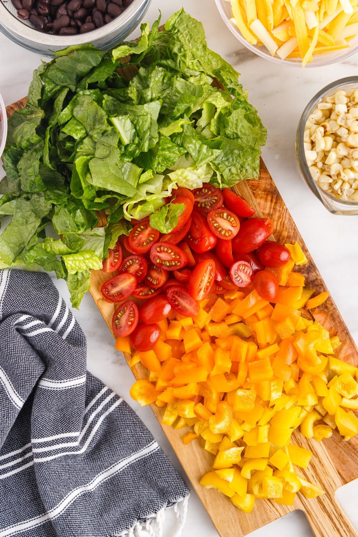 Diced lettuce, tomatoes, and peppers on a cutting board for the layered salad.