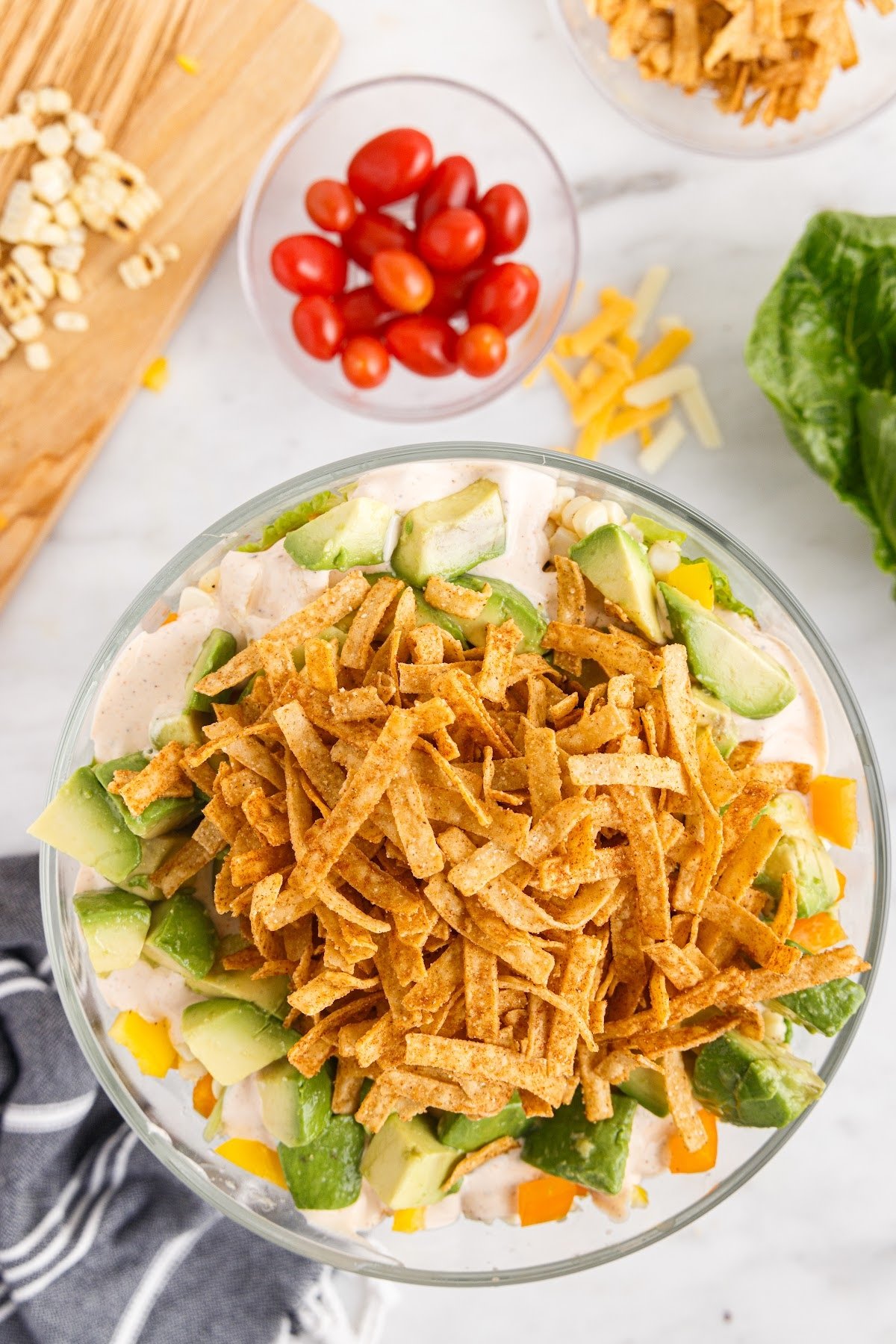 Topping the layered salad with tortilla strips and avocado.