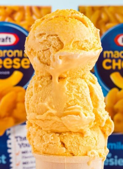 Stack of scoops of Copycat Mac and Cheese Ice Cream, with boxes of Mac and Cheese in the back ground.