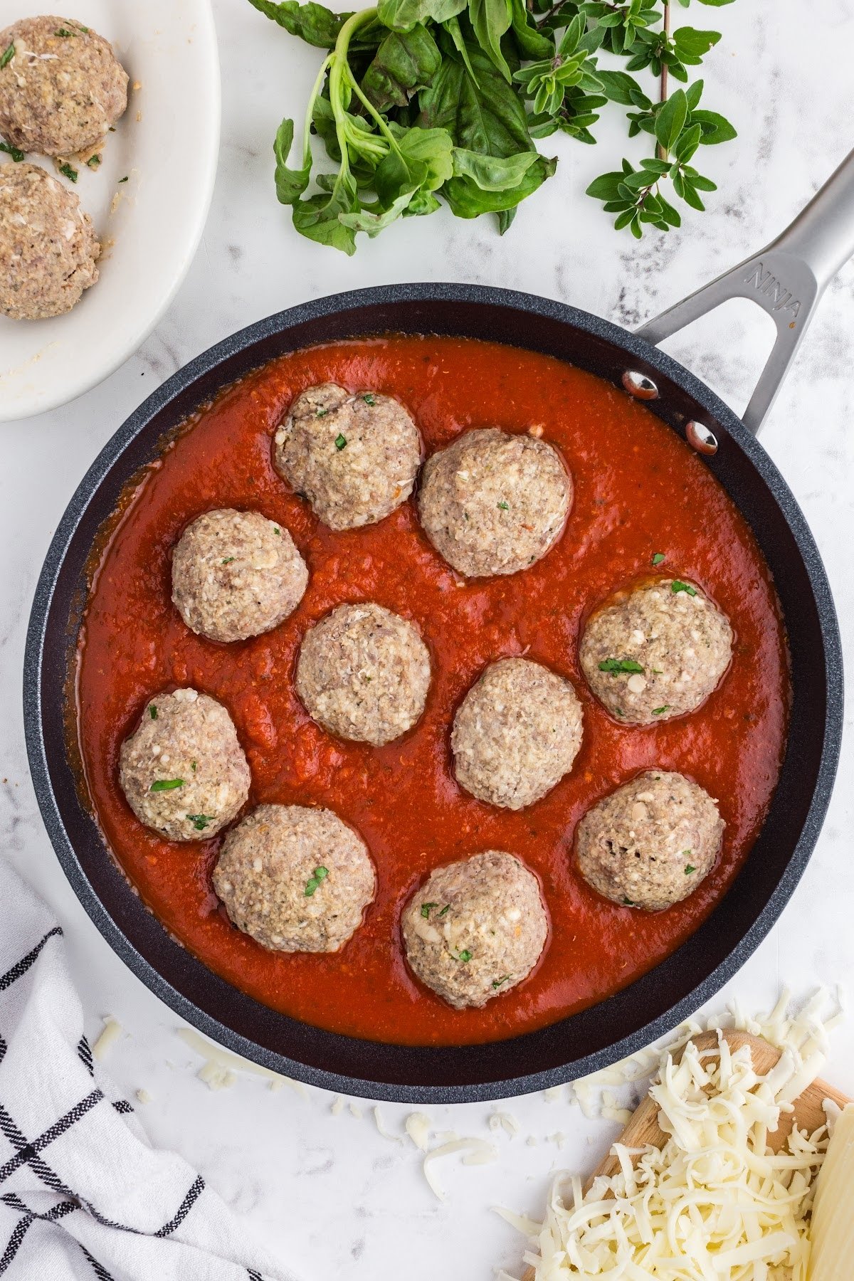 Meatballs in marinara sauce in a skillet on the stove, warming up.