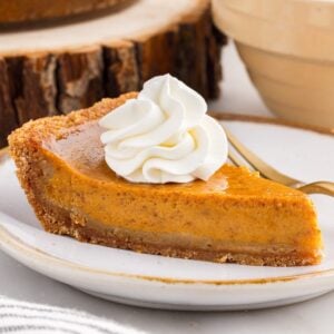 Homemade slice of pumpkin pie topped with whipped cream on a graham cracker crust.