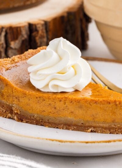 Homemade slice of pumpkin pie topped with whipped cream on a graham cracker crust.