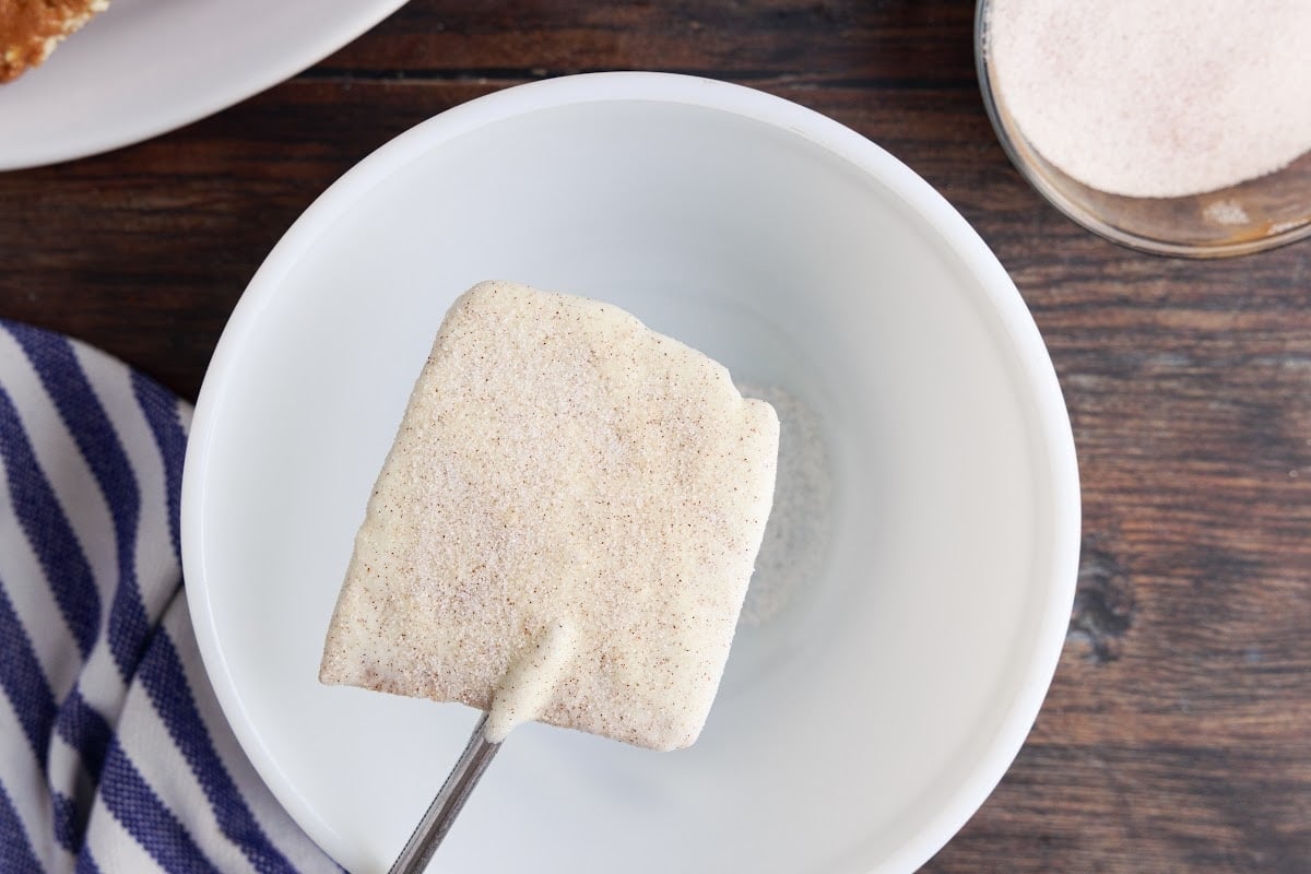 Holding the white chocolate covered toffee over a bowl while dusting with cinnamon and sugar.