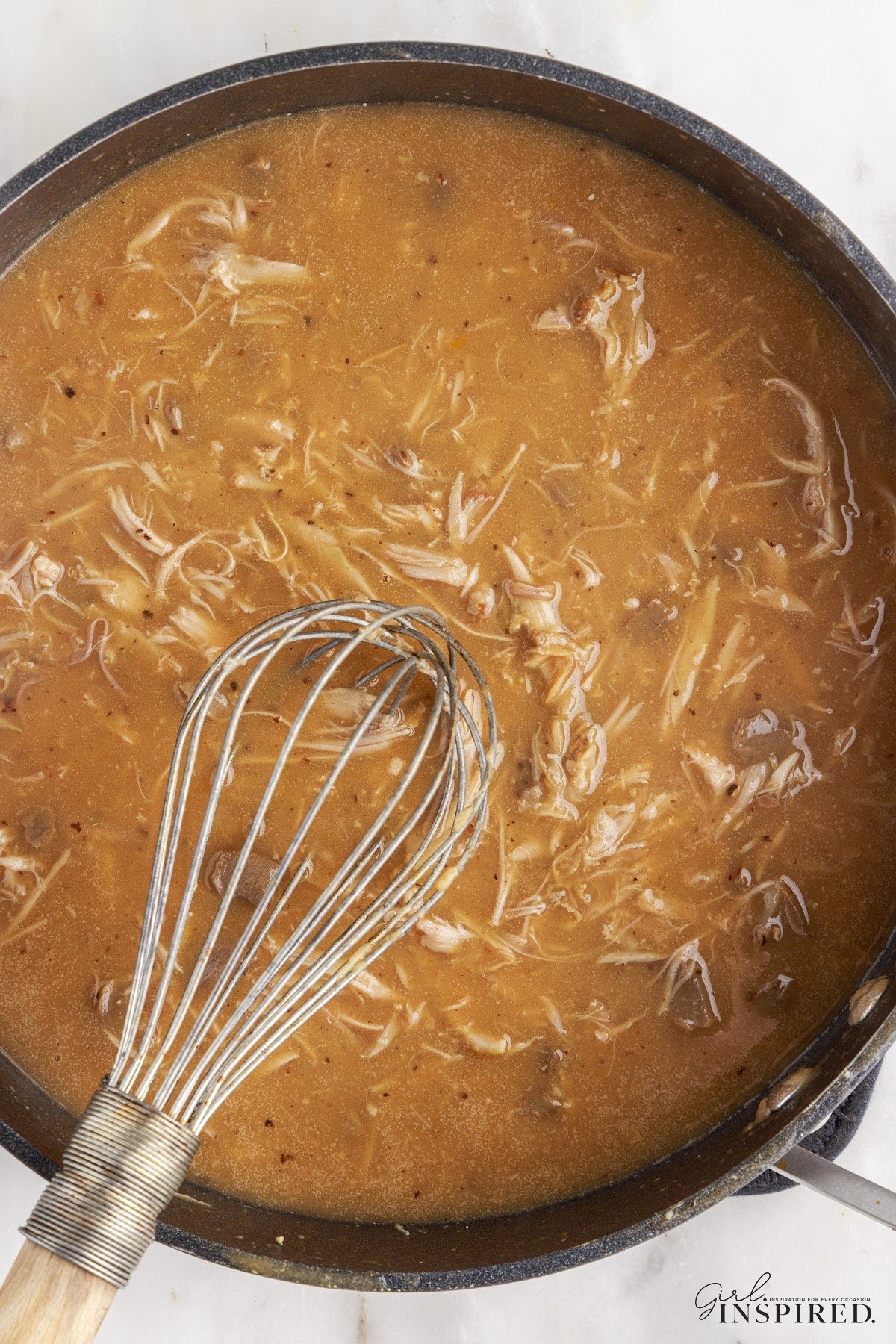 Overview of a large pot of Turkey neck gravy, with a whisk.