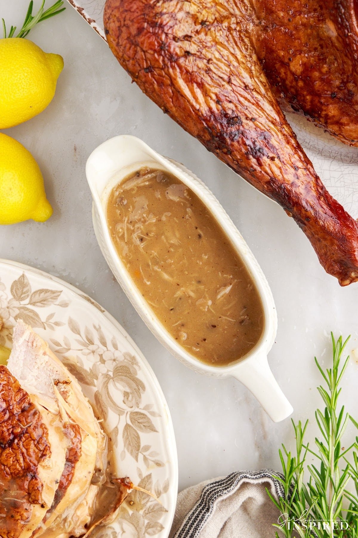 A boat of Turkey neck gravy next to a turkey leg and plate of food.