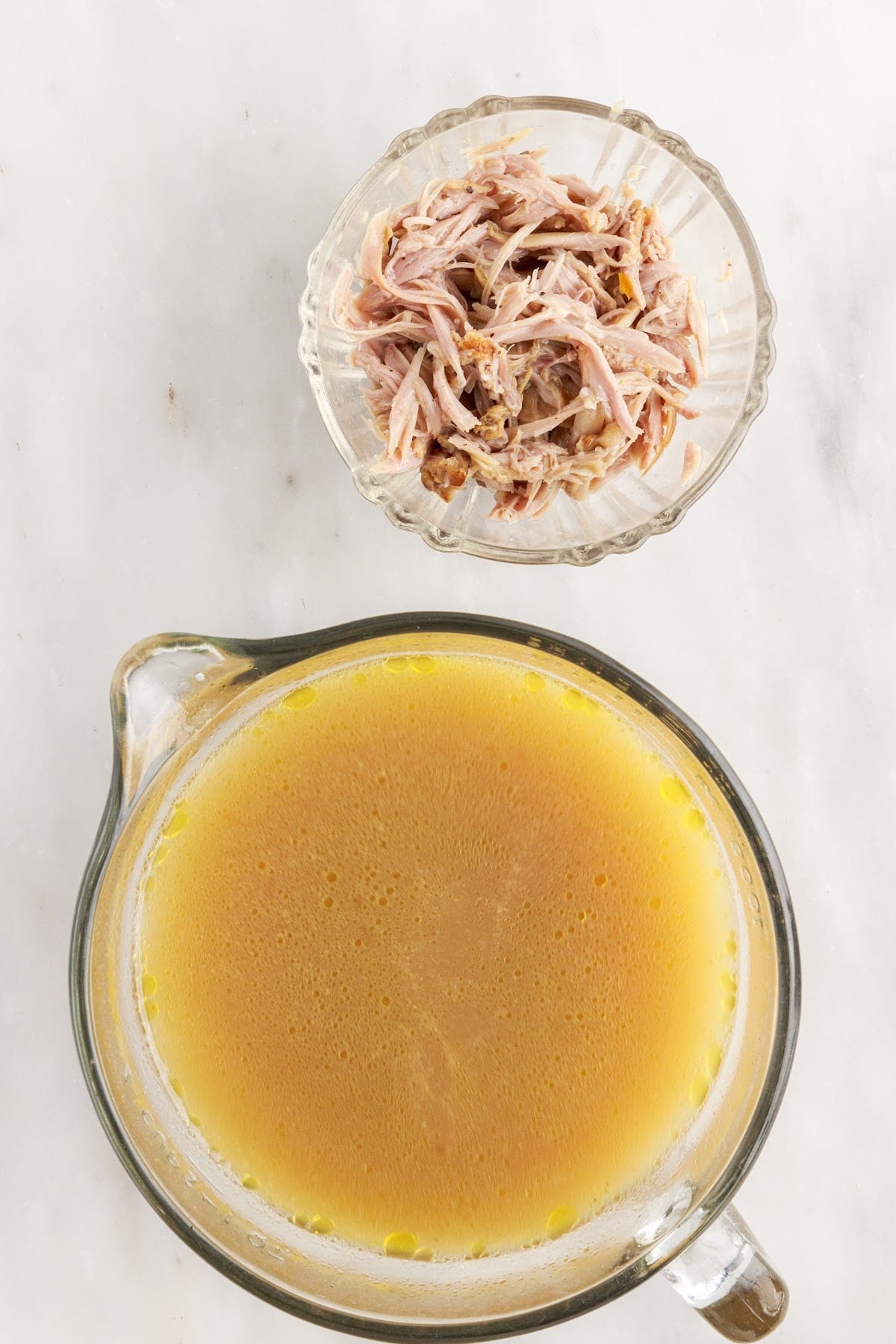 Turkey gravy liquids in  bowl with the meat from the neck in another bowl to the side.