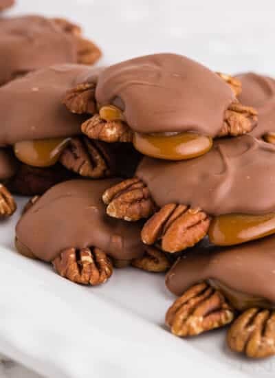 Close up of a stack of chocolate turtles on the counter, showing the pecans and chocolate covering.