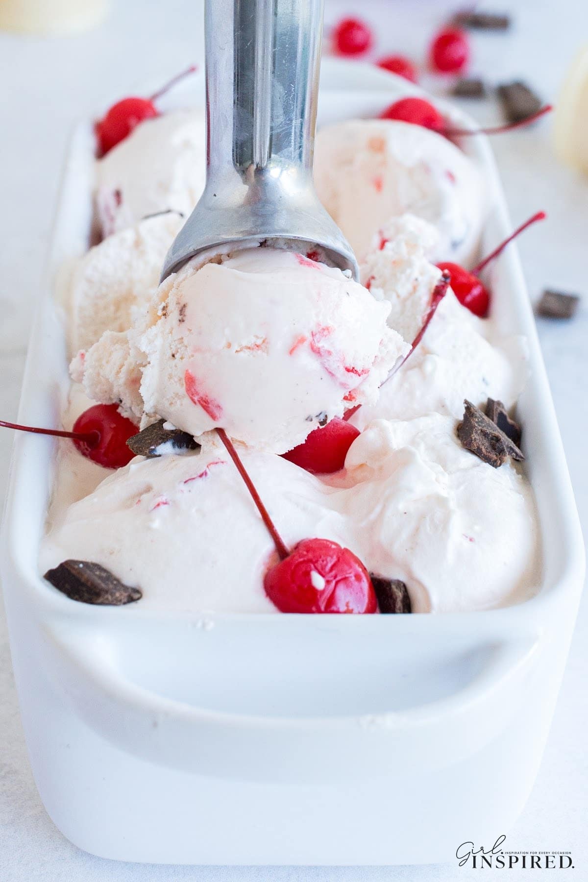 Scooping out cherry garcia ice cream with a metal scooper from the pan.