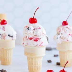 Three cones of cherry garcia ice cream with cherries on top.