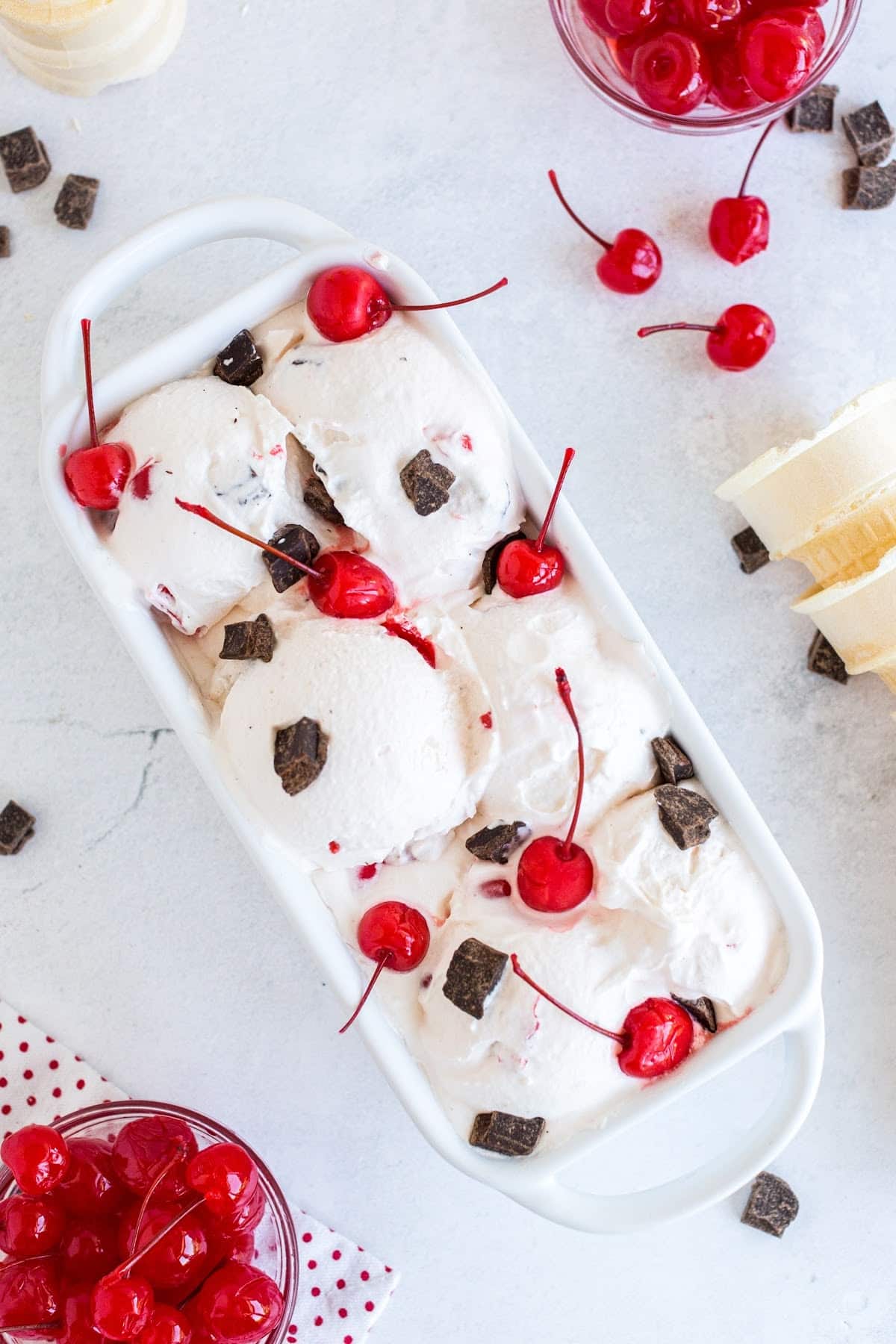 A loaf pan of homemade cherry garcia ice cream topped with cherries and chunks of chocolate.