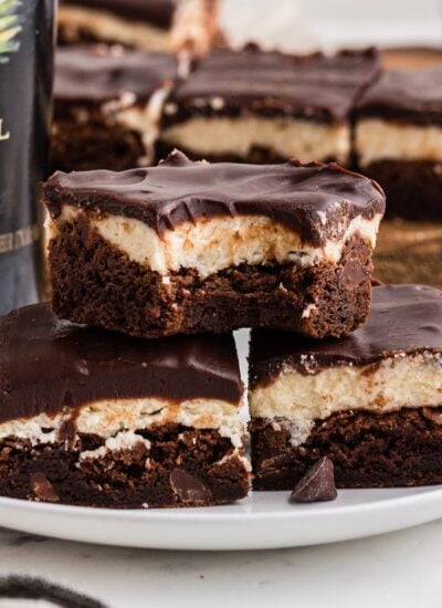 Stack of two Baileys Brownies with a bite taken out of the top one, other brownies in the background and text overlay.