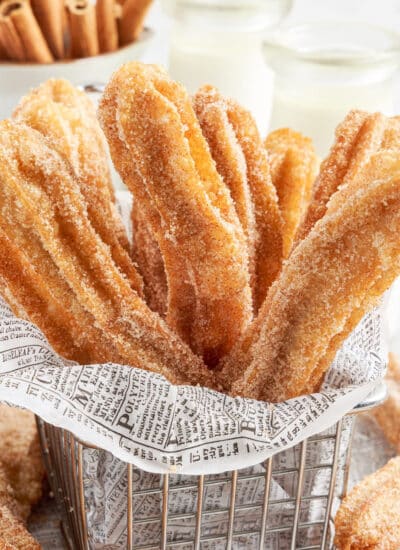 Bundle of Churro's in a basket, with text overlay and cinnamon sticks in the background.