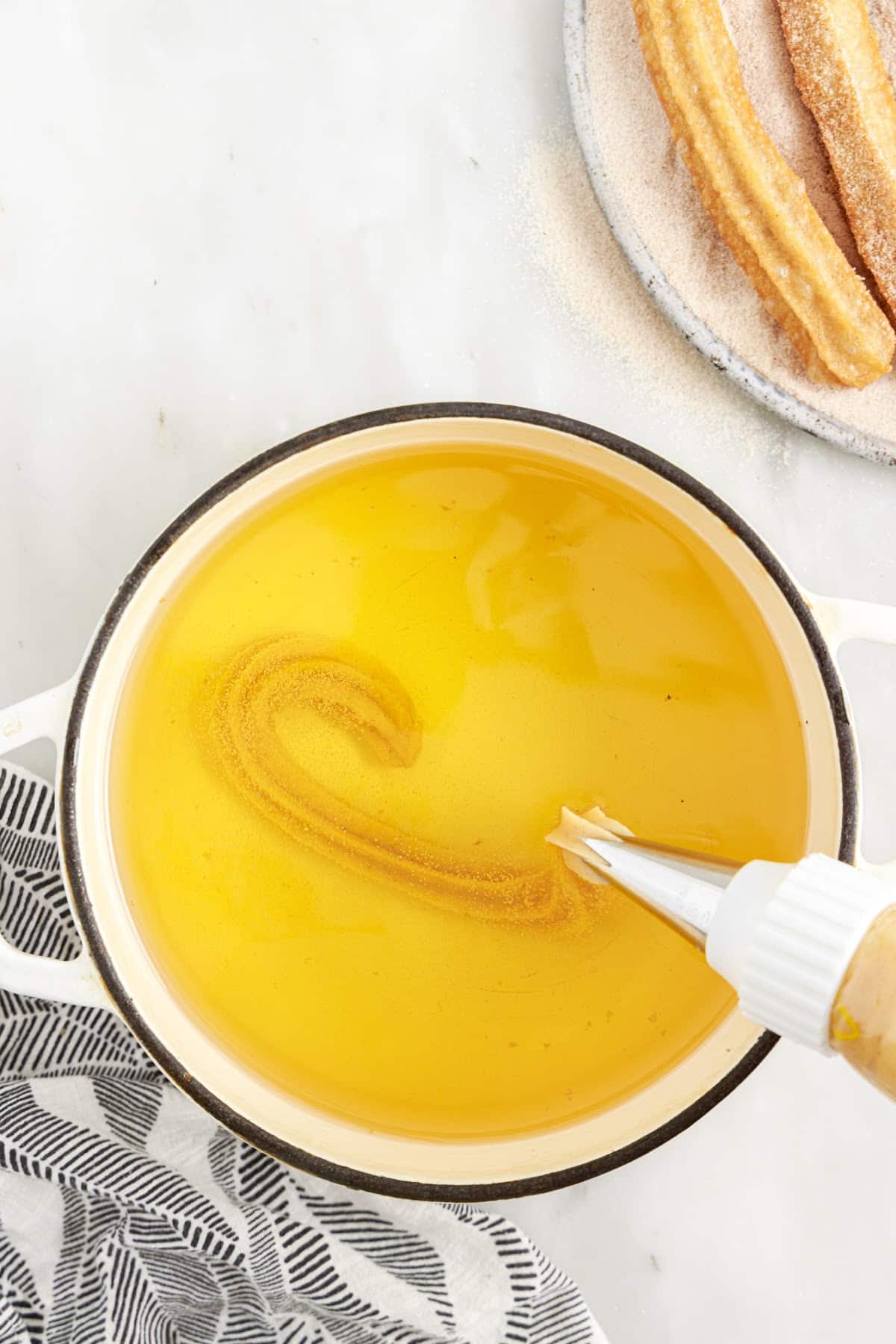 With a piping bag, placed churro batter into the heated oil, with churros off to the side.