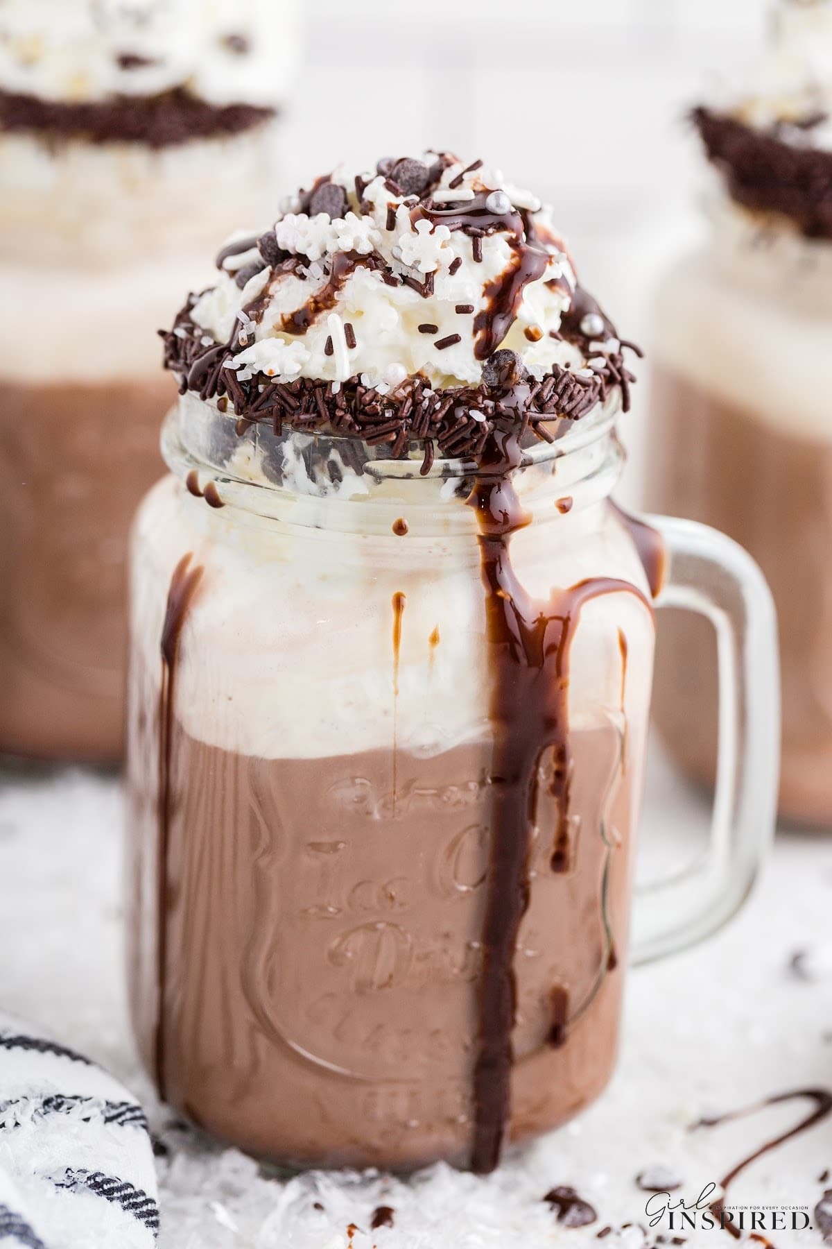 Close up of a Dirty Snowman drink with whipped cream and sprinkle garnishes, and other glasses in the background of dirty snowmen.